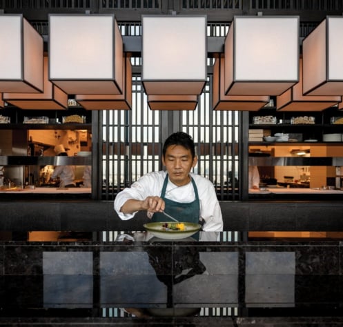 角形の照明の下でカウンターに立つ料理人